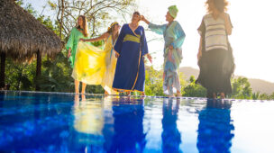 Grupo de mulheres sorrindo e se divertindo à beira de uma piscina em um cenário tropical ao entardecer, representando liberdade, bem-estar e conforto térmico.