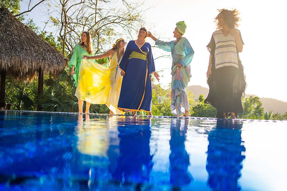 Grupo de mulheres sorrindo e se divertindo à beira de uma piscina em um cenário tropical ao entardecer, representando liberdade, bem-estar e conforto térmico.