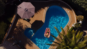 Vista aérea de uma piscina com mulher relaxando em boia inflável sob o sol, destacando o aproveitamento completo da área de lazer com conforto térmico garantido por bomba de calor.
