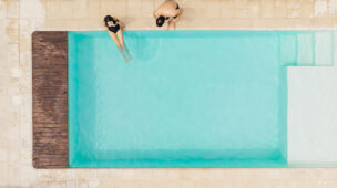 Vista aérea de duas pessoas na borda de uma piscina clara e moderna, desfrutando tranquilamente de um ambiente aquecido e agradável com o uso de bomba de calor.