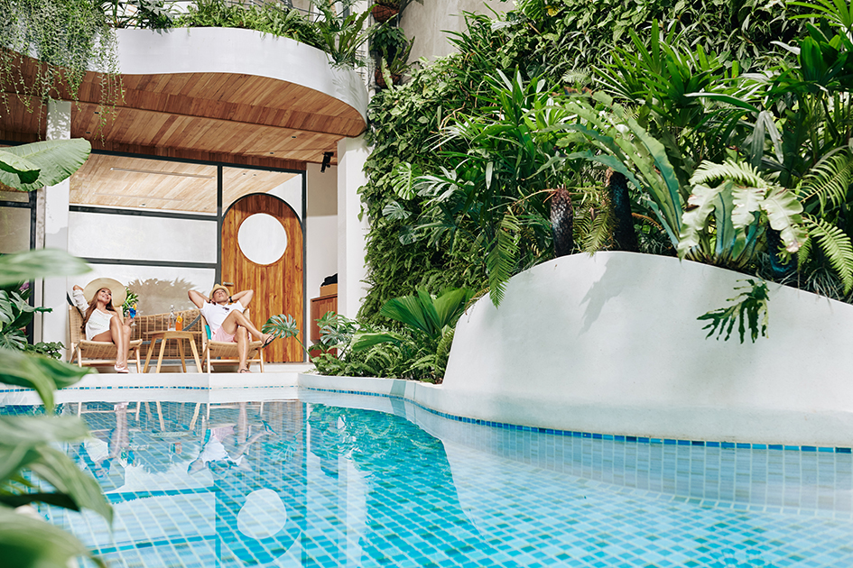 Casal relaxando em espreguiçadeiras ao lado de piscina cercada por vegetação tropical, aproveitando o conforto térmico garantido por trocador de calor Full Inverter.
