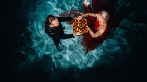 Casal elegante jogando xadrez dentro de uma piscina iluminada à noite, representando conforto térmico e experiências sofisticadas.