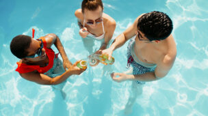 Três amigos brindando dentro de uma piscina clara, aproveitando momentos de lazer proporcionados por conforto térmico ideal com bomba de calor Full Inverter.