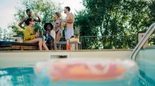 Grupo de jovens se divertindo ao lado da piscina, com bebidas e clima descontraído, aproveitando o conforto proporcionado por bomba de calor Full Inverter.