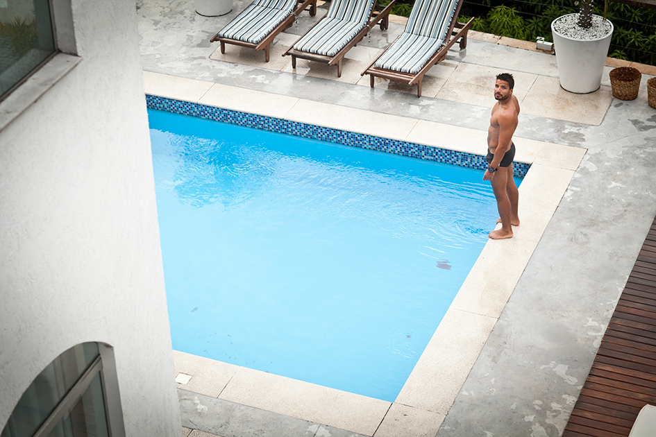 Homem ao lado de piscina residencial, observando a água em ambiente elegante com espreguiçadeiras, representando a importância do conforto térmico com bomba de calor.