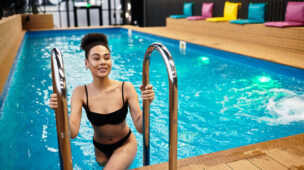 Mulher saindo da piscina aquecida em ambiente moderno e coberto, sorrindo e aproveitando o conforto térmico proporcionado por bomba de calor Full Inverter.